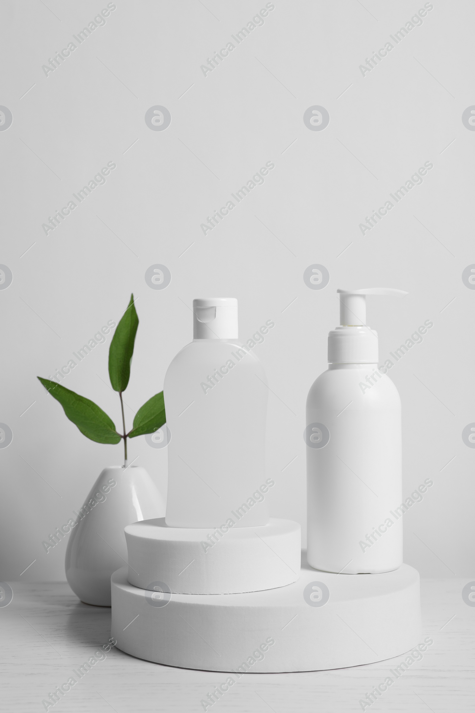 Photo of Bottles of cosmetic products and leaves on white wooden table
