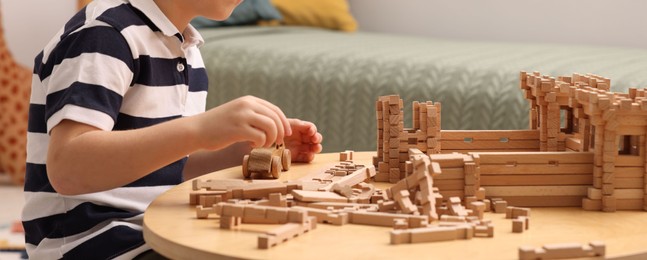 Photo of Little boy playing with wooden construction set at table indoors, closeup. Child's toy