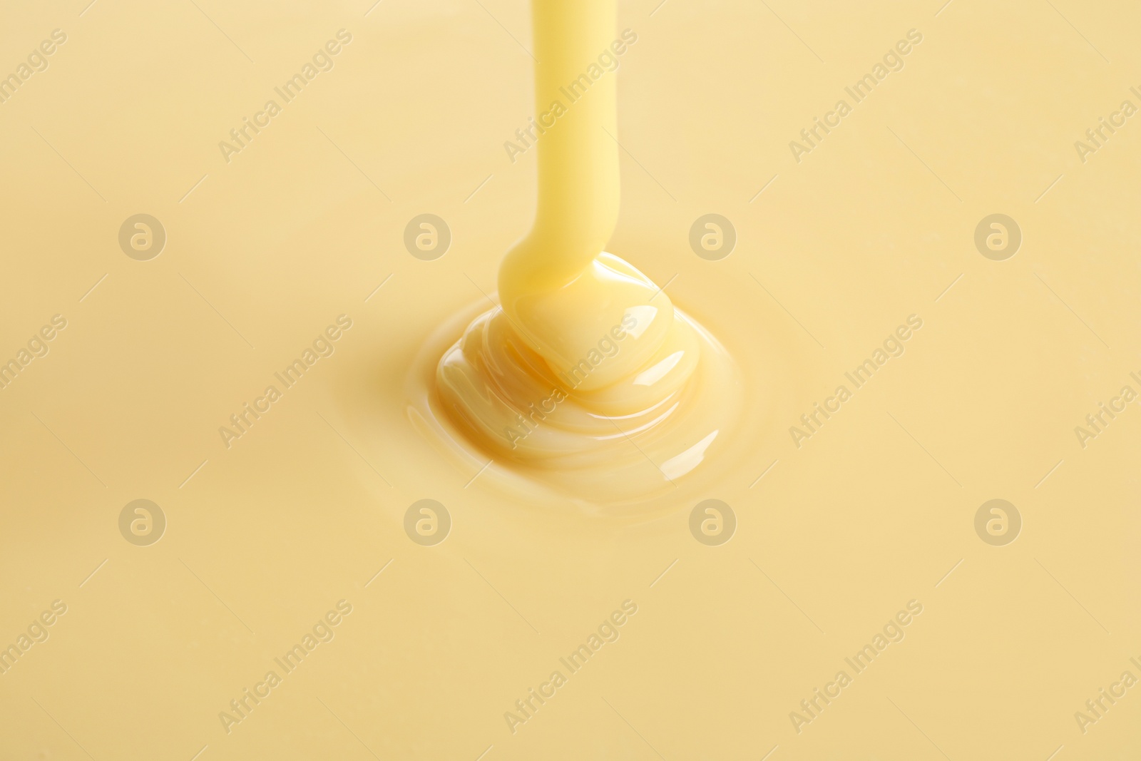 Photo of Tasty pouring condensed milk as background, closeup. Dairy product