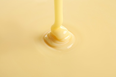 Photo of Tasty pouring condensed milk as background, closeup. Dairy product