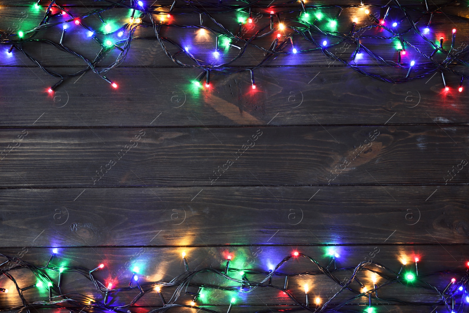 Photo of Glowing Christmas lights on dark wooden background, top view. Space for text