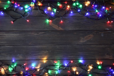 Photo of Glowing Christmas lights on dark wooden background, top view. Space for text