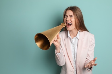 Young woman shouting into megaphone on color background