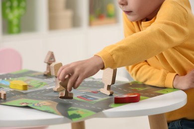 Photo of Little boy playing with set of wooden road signs and cars at table indoors, closeup. Child's toy