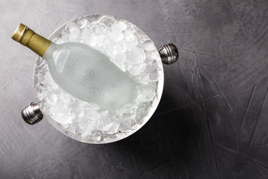 Bottle of vodka in metal bucket with ice on grey table, top view