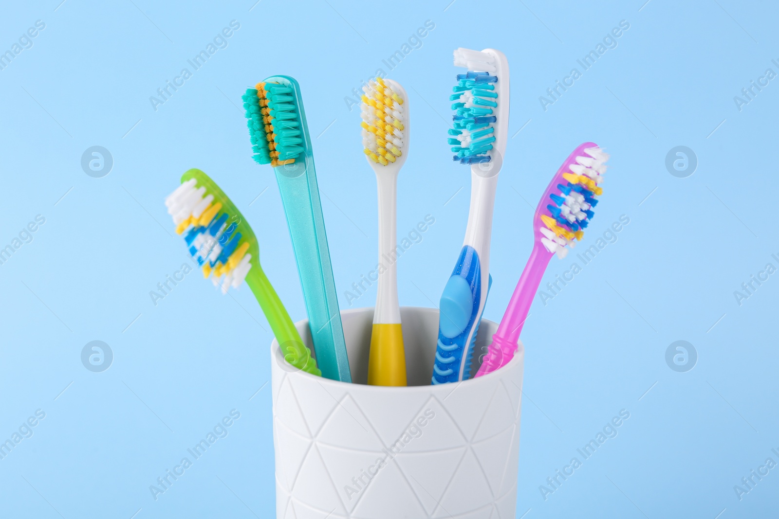 Photo of Different toothbrushes in holder on light blue background, closeup