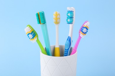 Photo of Different toothbrushes in holder on light blue background, closeup