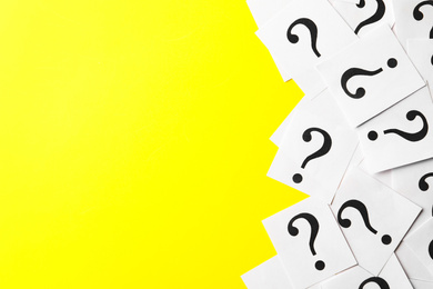 Photo of Paper notes with question marks on yellow background, flat lay. Space for text