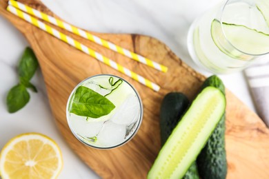 Photo of Tasty fresh cucumber water with sliced lemon and basil on white table, flat lay