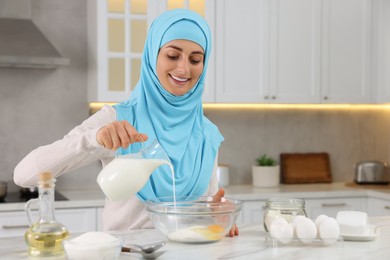 Photo of Muslim woman making dough at white table in kitchen