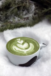 Cup of fresh matcha latte in snow outdoors
