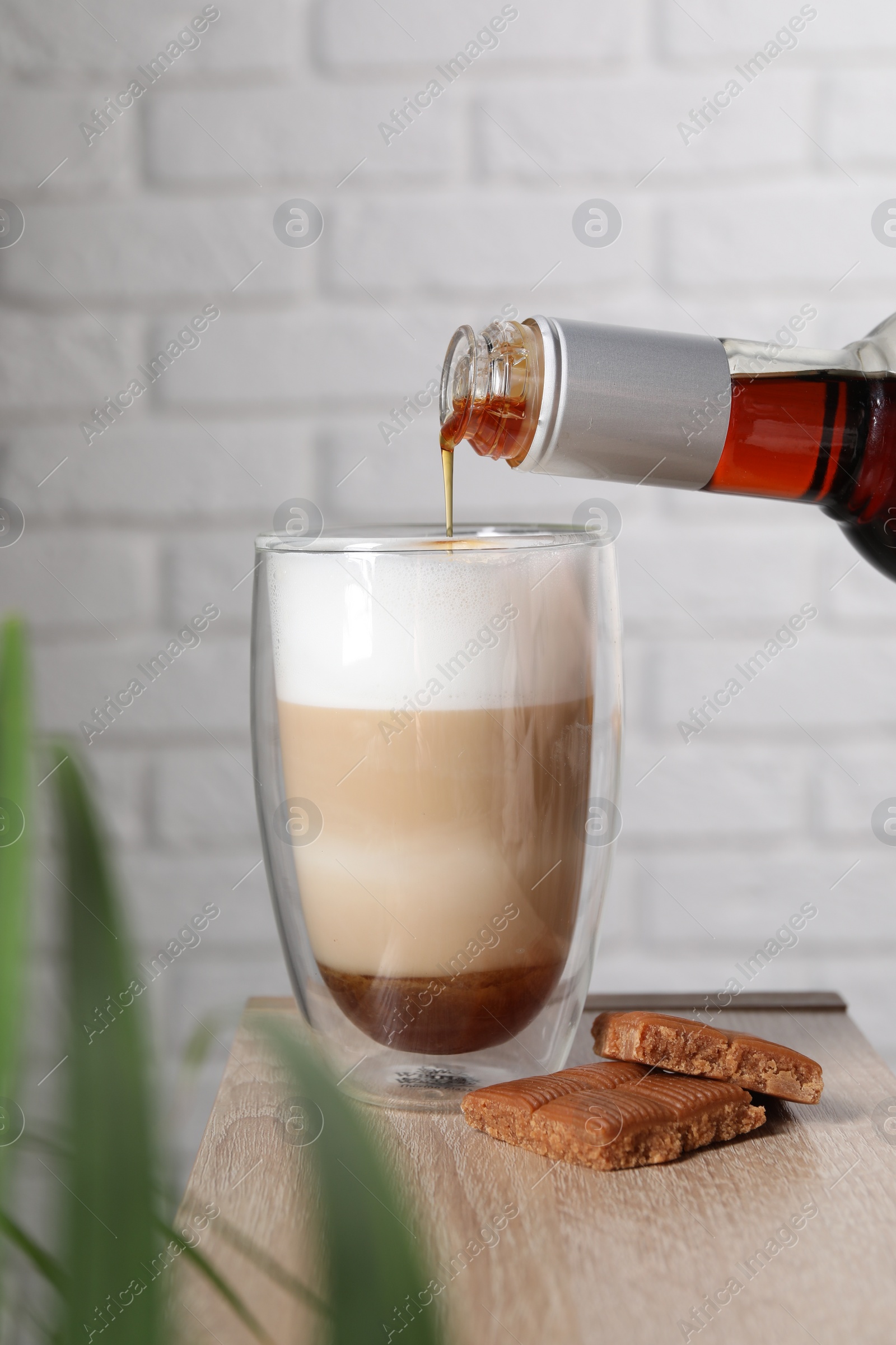 Photo of Pouring syrup into glass of tasty coffee on wooden table