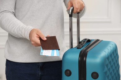 Photo of Tourist with suitcase giving passport and tickets on blurred background, closeup