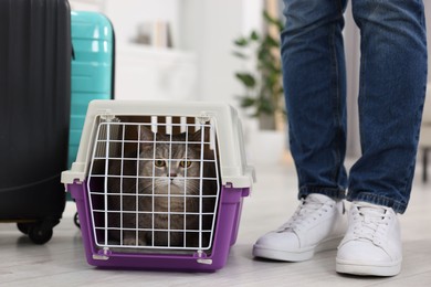 Photo of Travel with pet. Man near carrier with cute cat at home, closeup