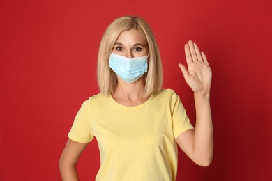Photo of Woman in protective mask showing hello gesture on red background. Keeping social distance during coronavirus pandemic
