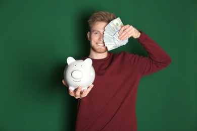Young man with piggy bank and money on color background