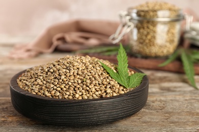 Photo of Bowl of hemp seeds on wooden table against color background