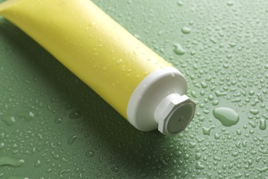 Photo of Moisturizing cream in tube on green background with water drops, closeup