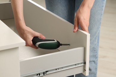 Woman with electric screwdriver assembling drawer, closeup