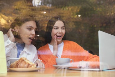 Special Promotion. Emotional young women using laptop at table in cafe, view from outdoors