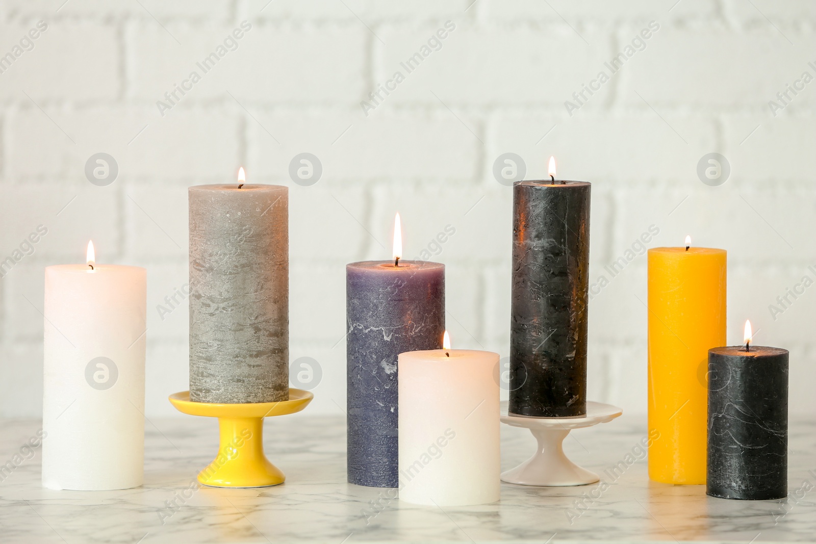 Photo of Different decorative wax candles on table against brick wall