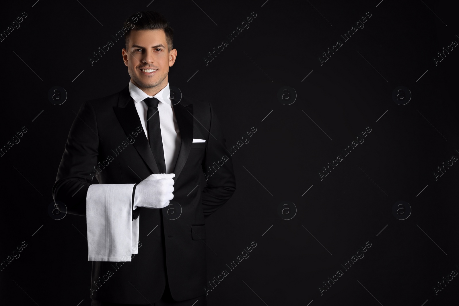 Photo of Handsome butler with towel on black background, space for text