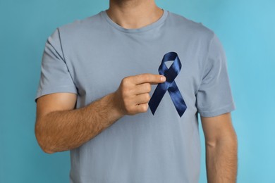 Photo of Man with ribbon on light blue background, closeup. Urology cancer awareness