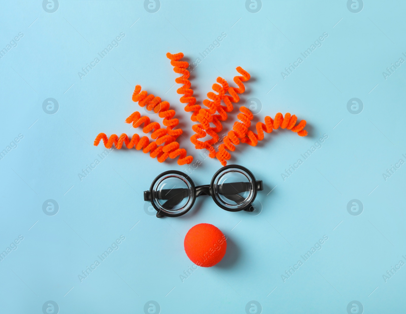 Photo of Funny face made with clown's accessories on light blue background, flat lay