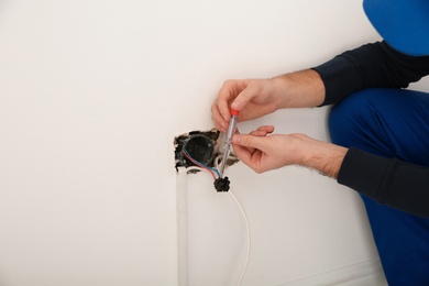 Electrician with neon-lamp tester checking voltage indoors, closeup. Space for text