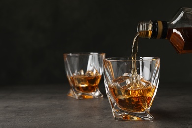 Photo of Pouring whiskey from bottle into glass with ice cubes on table. Space for text