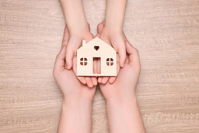 Photo of Home security concept. Man with his little child holding house model at wooden table, top view