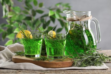 Glasses and jug of homemade refreshing tarragon drink with lemon slices on table