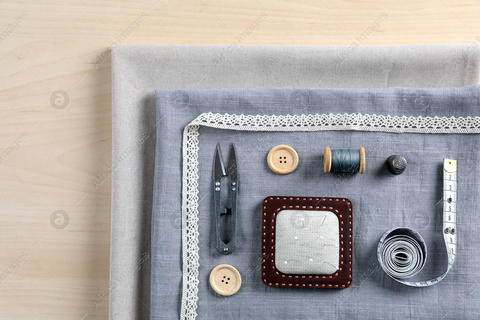 Photo of Set of sewing supplies and accessories with fabric on wooden table, top view