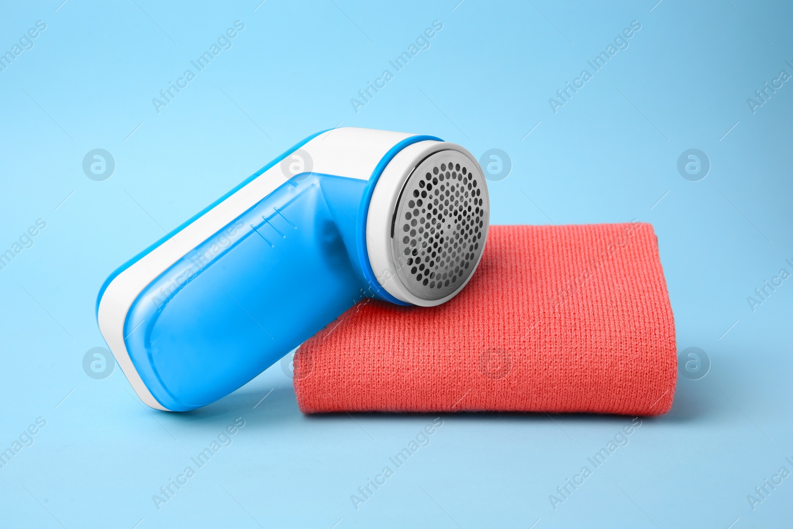 Photo of Modern fabric shaver and cloth with lint on light blue background