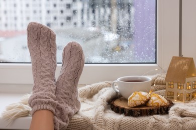 Woman in knitted socks relaxing near window at home, closeup. Space for text
