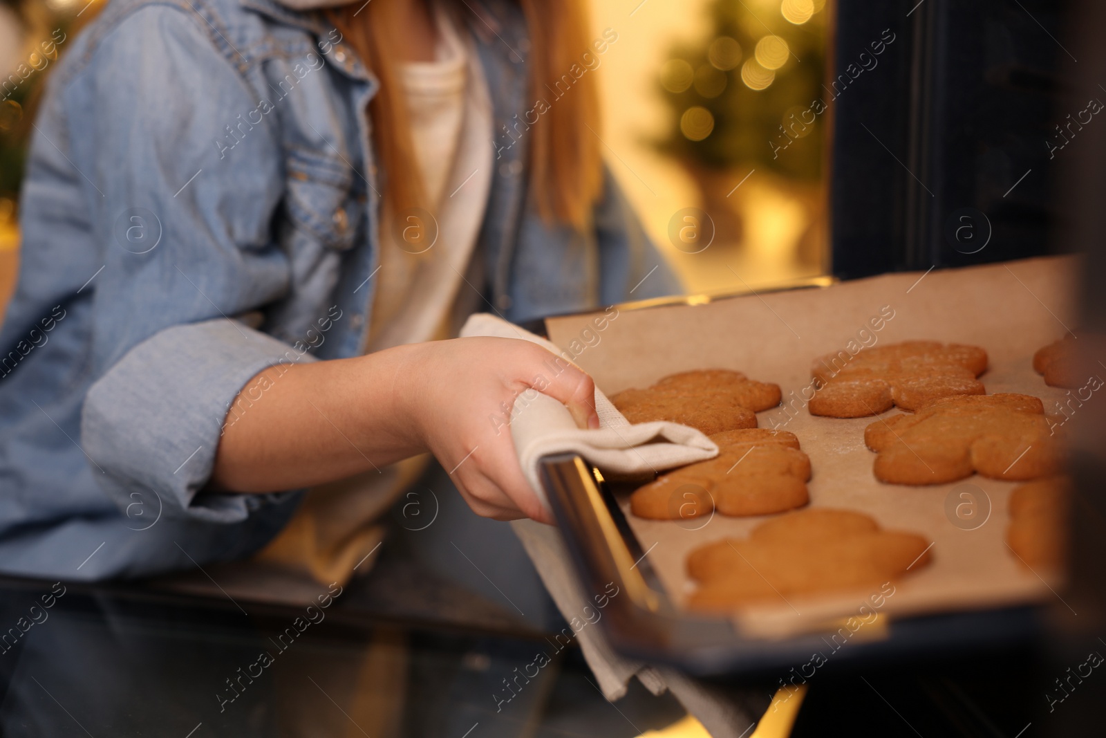 Photo of Little child taking baking sheet with Christmas cookies out of oven indoors, closeup