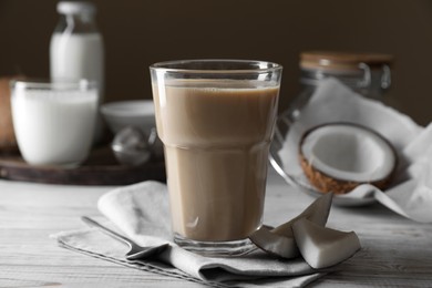 Glass of coffee with coconut milk and nut pieces on white wooden table, closeup