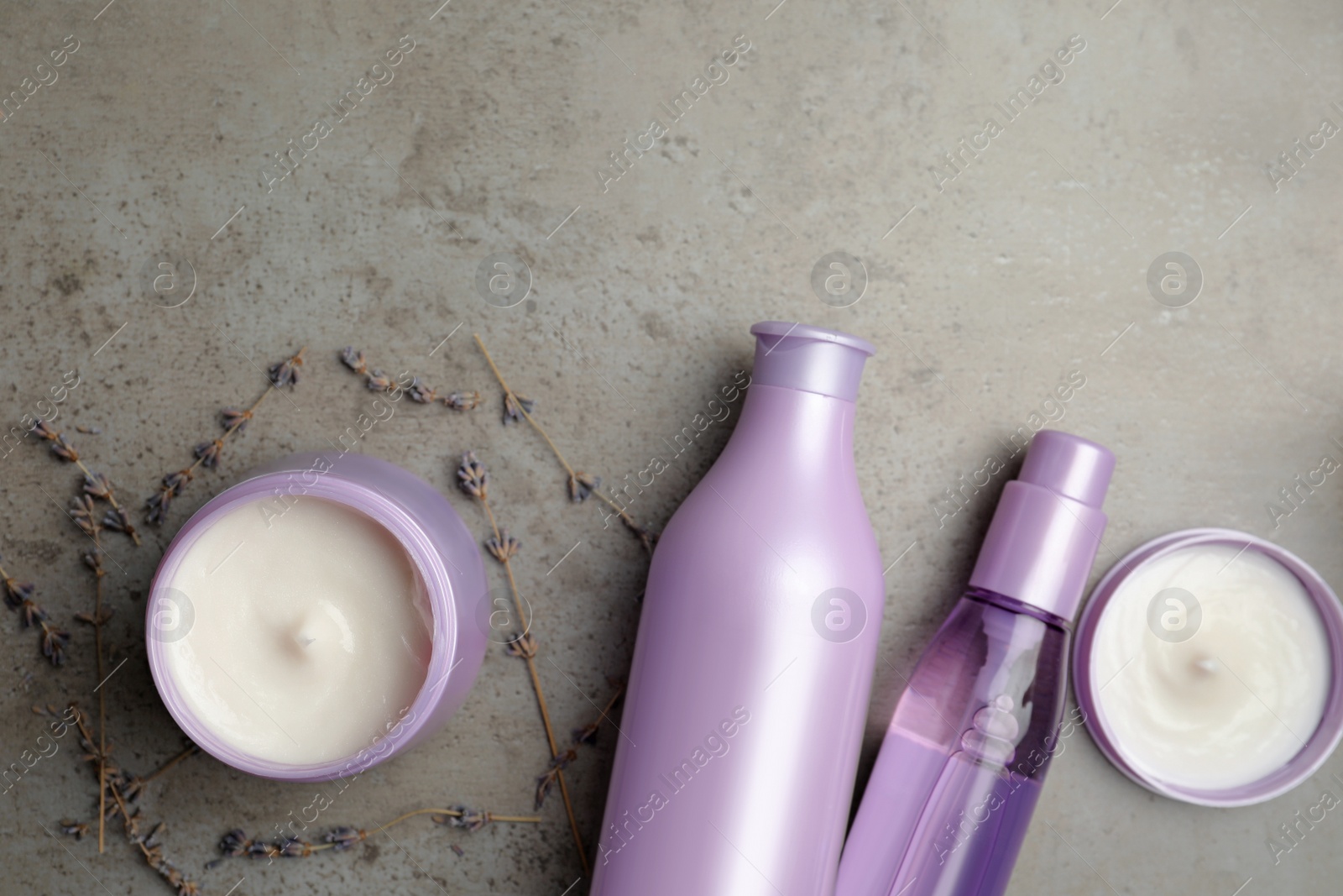 Photo of Set of hair care cosmetic products and dry lavender flowers on grey stone table, flat lay