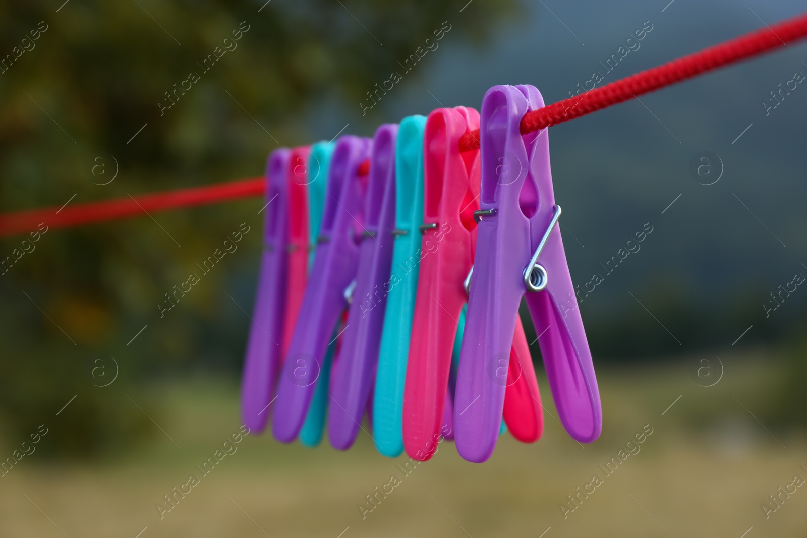 Photo of Colorful clothespins hanging on washing line outdoors, closeup