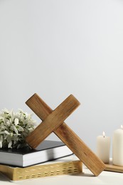 Photo of Wooden cross, ecclesiastical books, church candles and flowers on white table