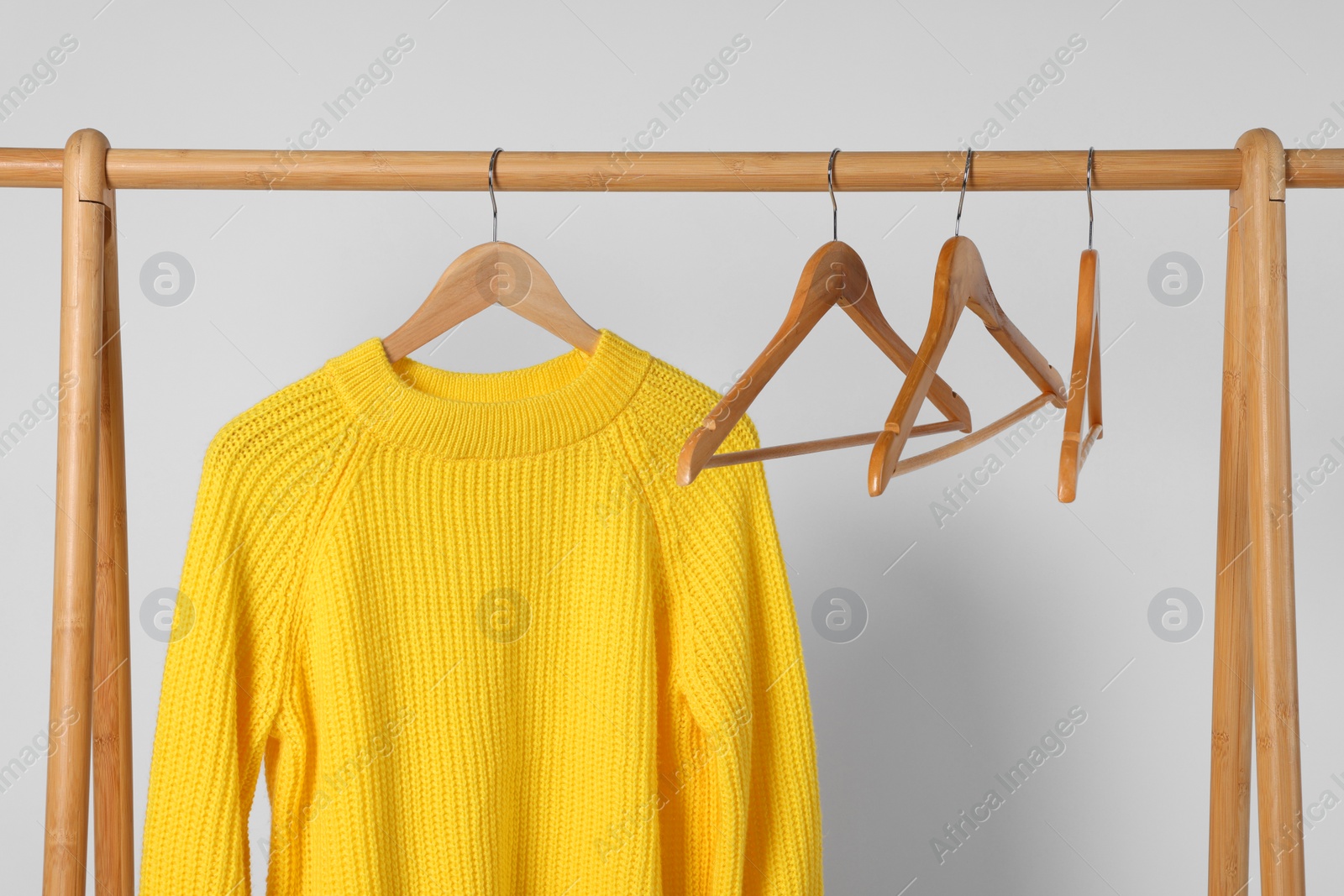 Photo of Rack with yellow knitted sweater and hangers on light background