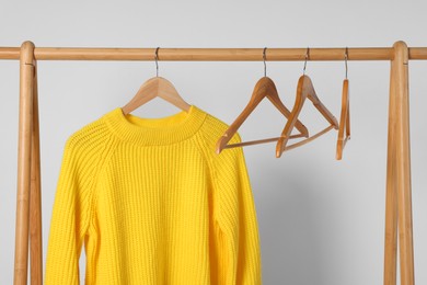 Photo of Rack with yellow knitted sweater and hangers on light background