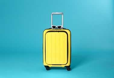 Photo of Stylish suitcase with sunglasses on color background