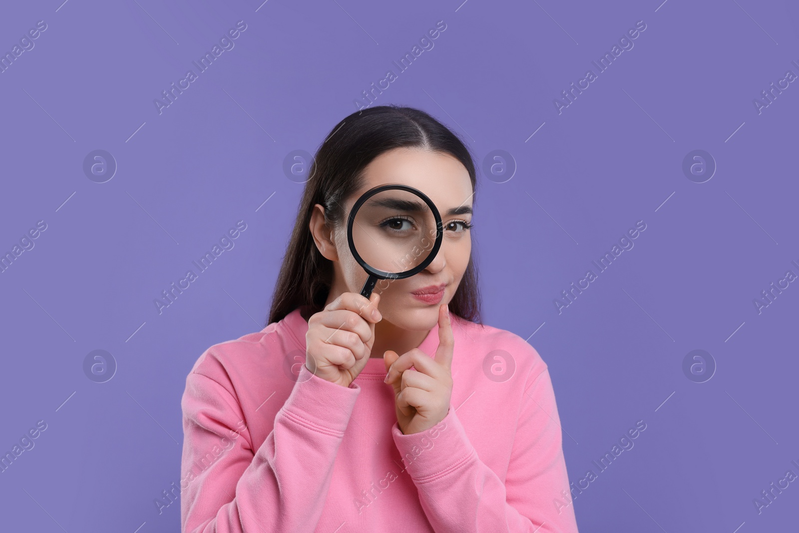 Photo of Confused young woman looking through magnifier glass on purple background