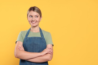 Photo of Beautiful young woman in denim apron on orange background. Space for text