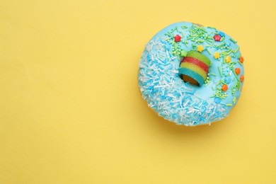 Photo of Glazed donut decorated with sprinkles on yellow background, top view. Space for text. Tasty confectionery