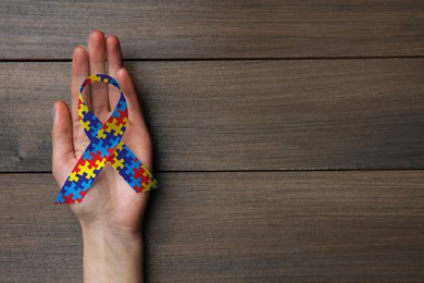 World Autism Awareness Day. Woman with colorful puzzle ribbon on wooden background, top view with space for text