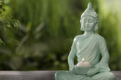 Buddhism religion. Decorative Buddha statue with burning candle on table outdoors, space for text