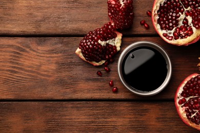 Photo of Glass bowl of tasty pomegranate sauce and fresh ripe fruit on wooden table, flat lay. Space for text