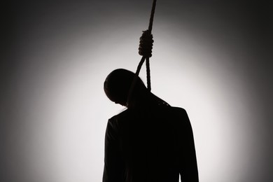 Silhouette of woman with rope noose on neck against light background, back view